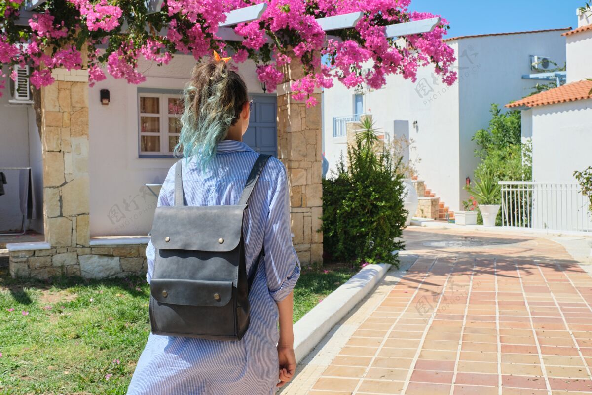 美女时尚时尚的蓝发女孩背着背包 在阳光明媚的夏日漫步于度假村 沿着棕色瓷砖路面漫步 背影空间女人模特女孩