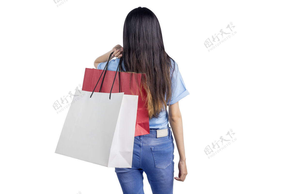 控股背着购物袋隔着白墙的亚洲女人的后视图女性顾客快乐