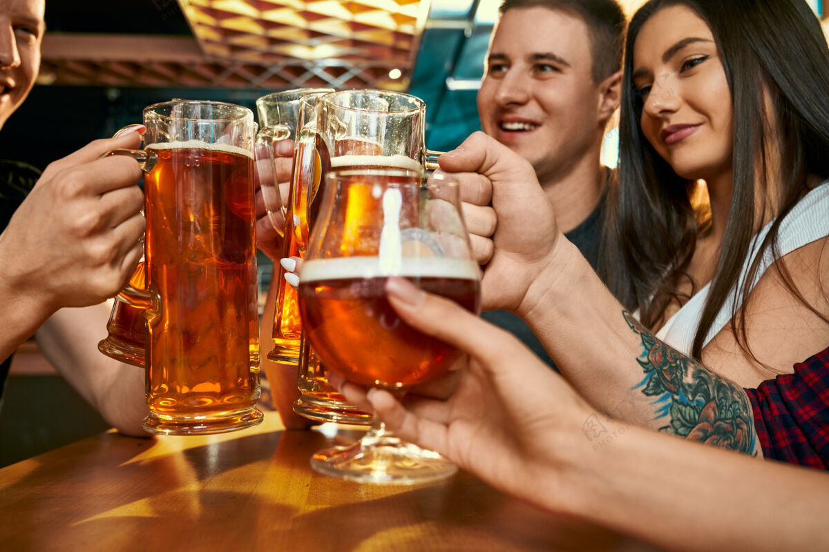 乐趣在酒吧里 快乐的年轻朋友们手里拿着一品脱啤酒起草成人人