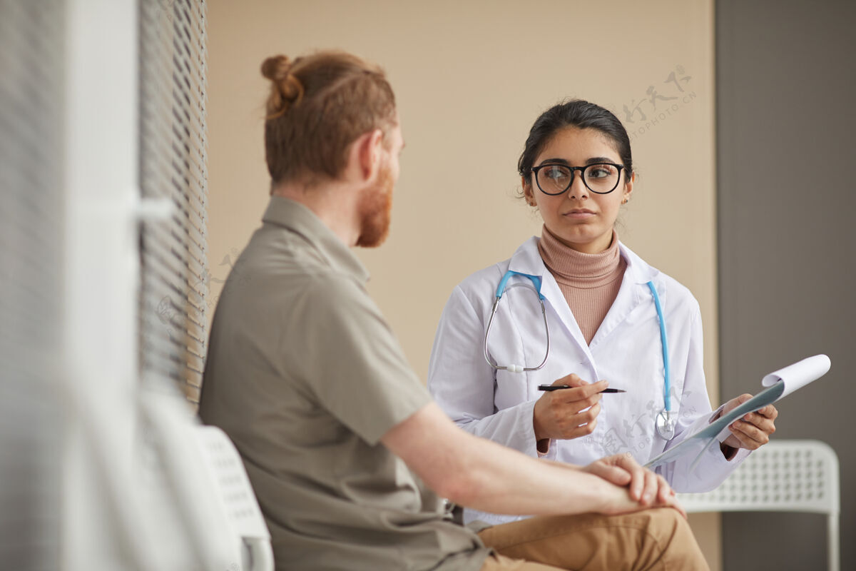 成人年轻的女医生拿着名片 坐在走廊里和病人讨论他的病医生看诊所