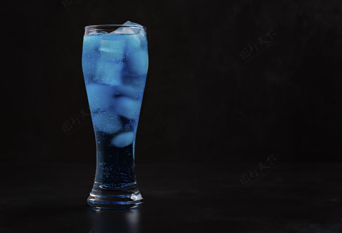 饮料高玻璃杯里放着冰块的蓝色鸡尾酒站在黑暗中蓝色鸡尾酒热量酒精鸡尾酒