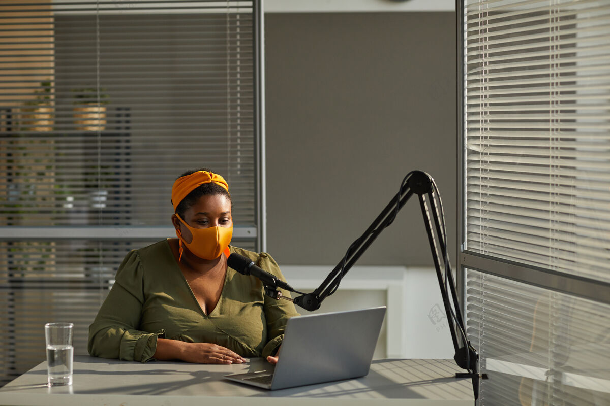收音机戴着防护面具的年轻女子在直播过程中用笔记本电脑在线接受采访现代通信办公桌