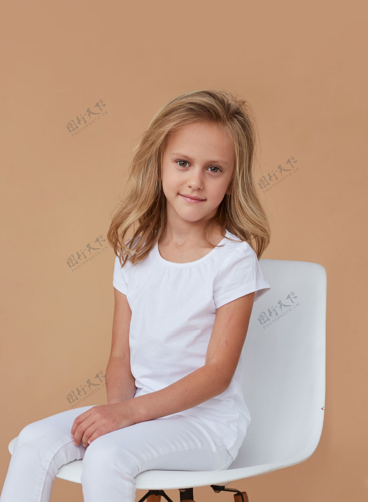 快乐前面的肖像是一个美丽的微笑的小女孩 卷曲的金发 穿着白衣服 坐在椅子上孩子年轻白布