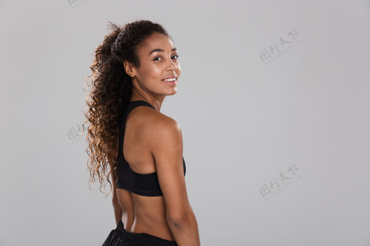 人一个微笑的年轻非洲女运动员在灰色的墙上孤立的后视图肖像美国人健身女孩
