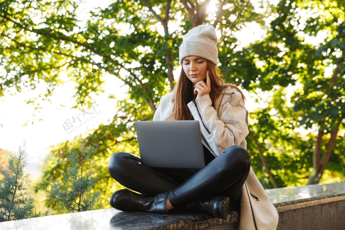 社交美丽的年轻女子穿着秋大衣 戴着秋帽坐在户外 用笔记本电脑休闲女孩使用