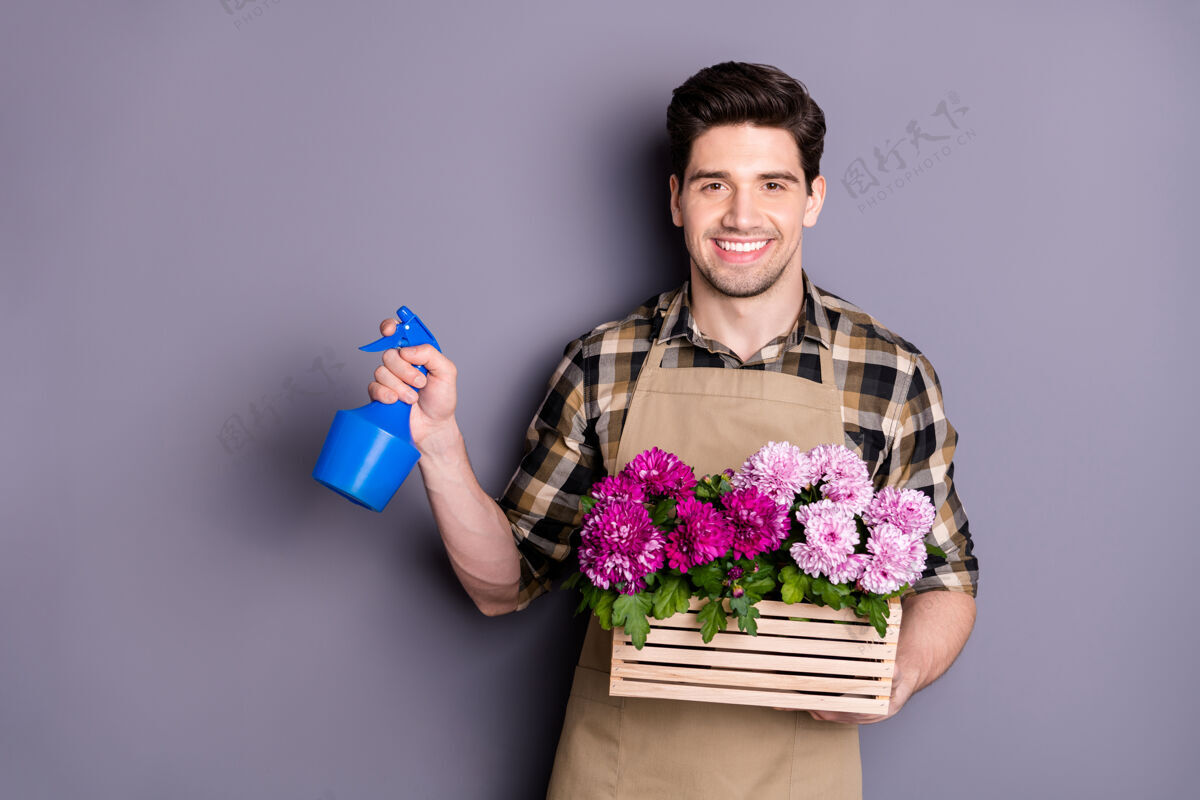 新鲜正面开朗男子肖像花店工人有自己的小花园关心植物花卉喷雾器穿格子衬衫隔离灰色墙壁花店职业商店