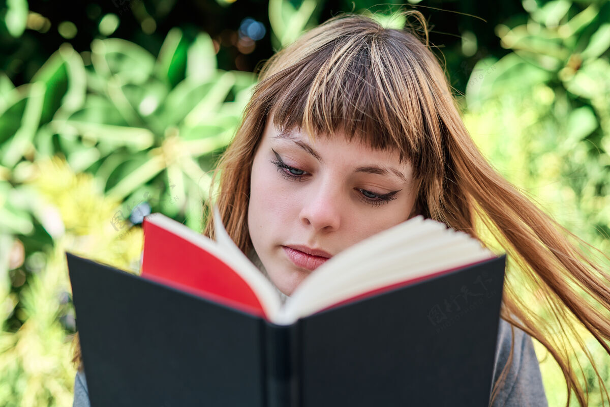 年轻一张蓝眼睛的白人金发年轻女子在公园看书的特写照肖像花园阅读