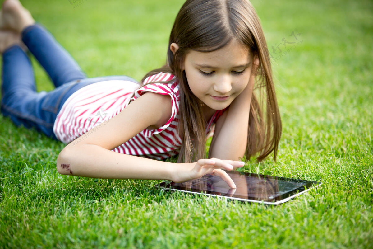 女孩可爱的女孩在草地公园使用数字平板电脑的肖像触摸屏休闲聪明