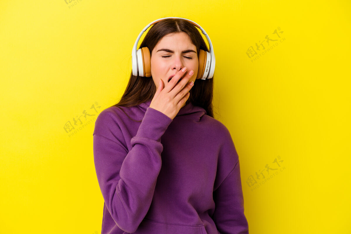 平静年轻的高加索女性戴着粉色背景的耳机听音乐 打着哈欠 用手捂着嘴疲惫手势女性