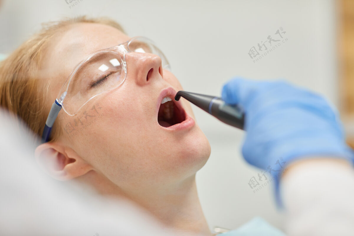 专业职业戴着护目镜的女病人躺着 眼睛闭着 嘴巴张开 牙医正在给她治牙保持人成人