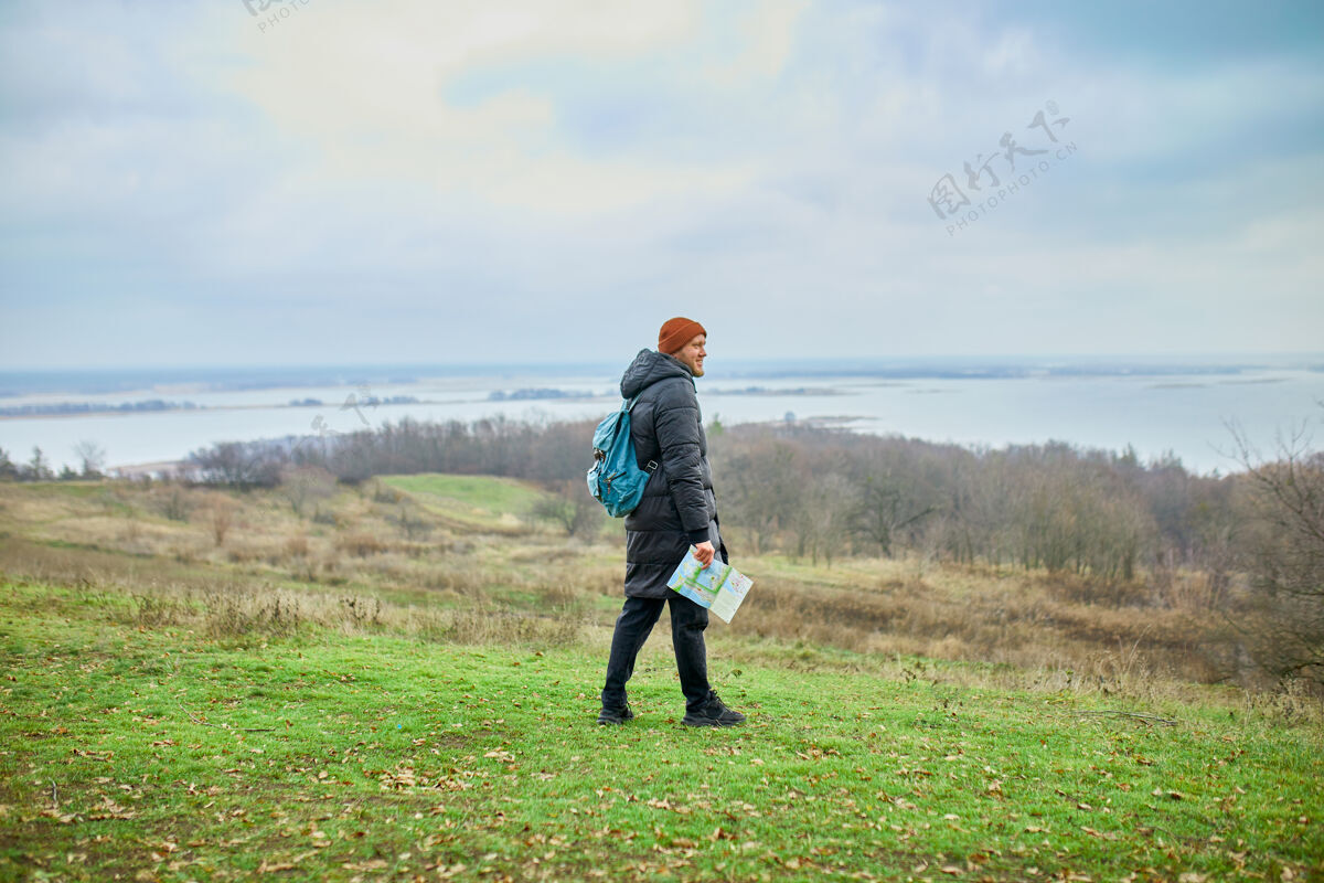 健康旅行家男人背着背包 手拿地图 在一堵自然的山河上 旅游的概念 度假和徒步旅行的生活方式的概念可持续的生活方式度假户外