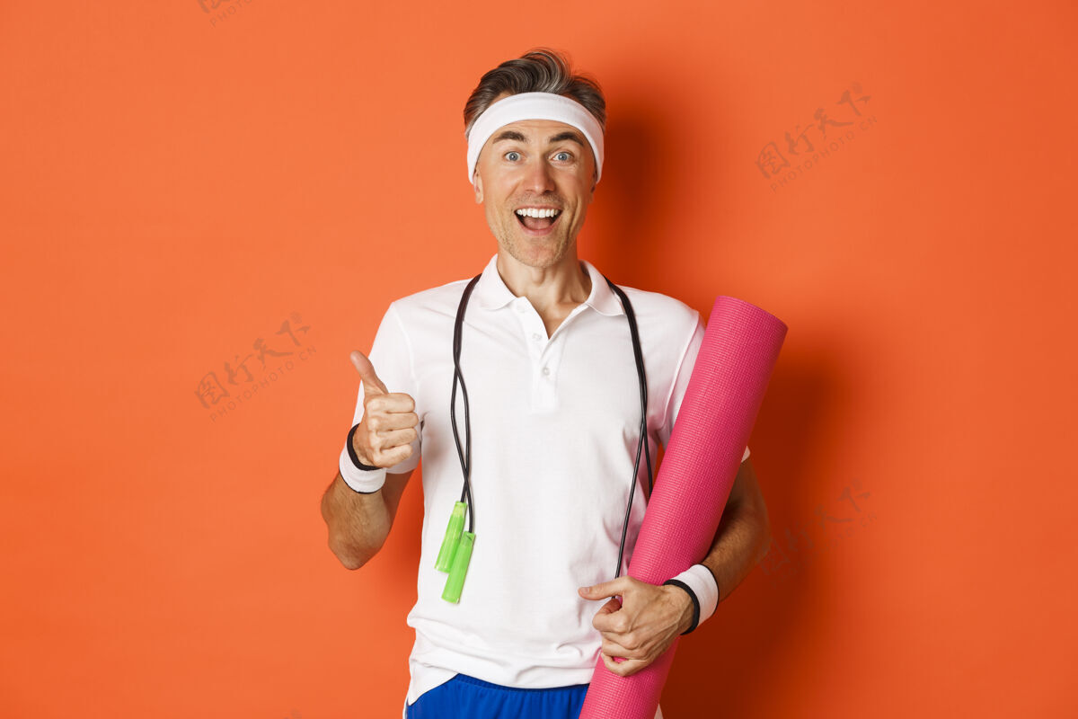 健身快乐的中年健身男 拿着跳绳和瑜伽垫同意拇指人