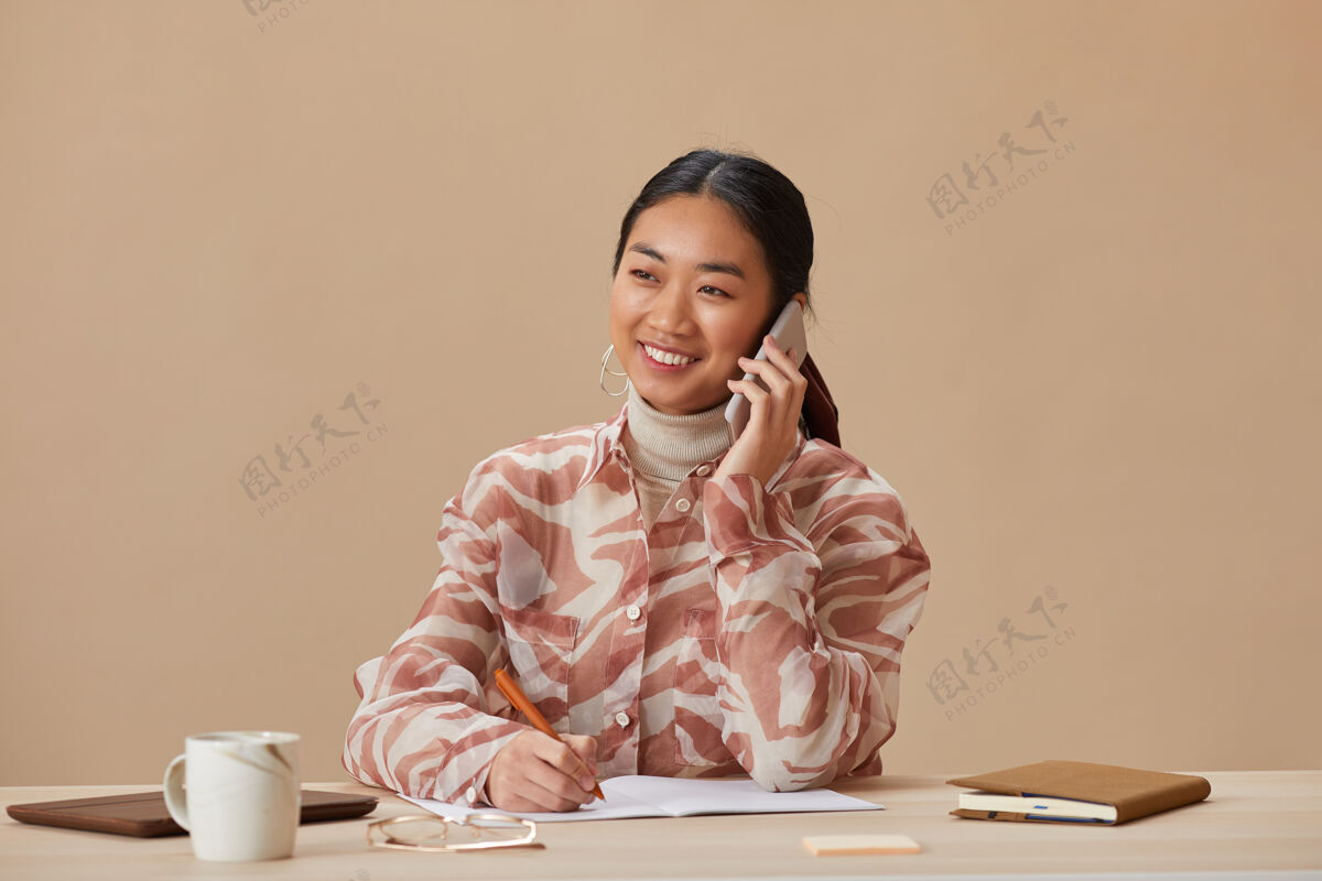 电话坐在桌边讲手机的亚洲女人的画像移动抱着欢呼