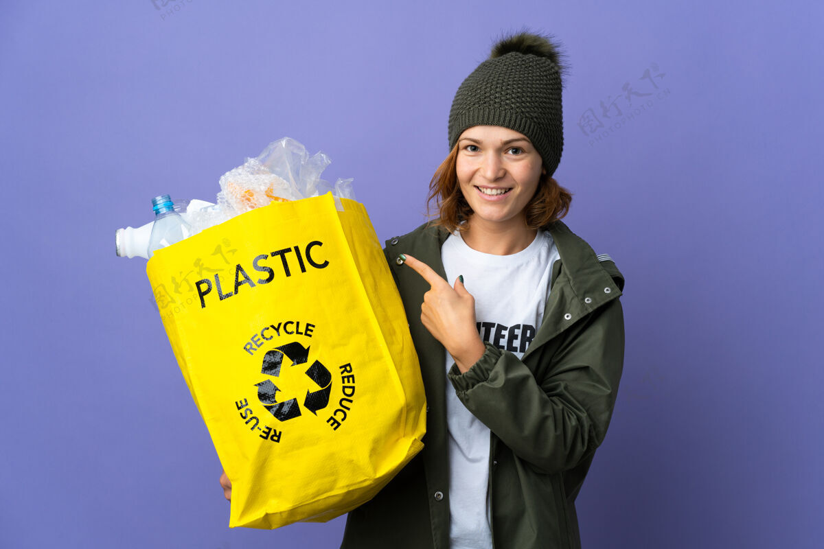 回收年轻的格鲁吉亚女孩拿着一个装满塑料瓶的袋子指着旁边的回收站赠送产品表情女孩塑料