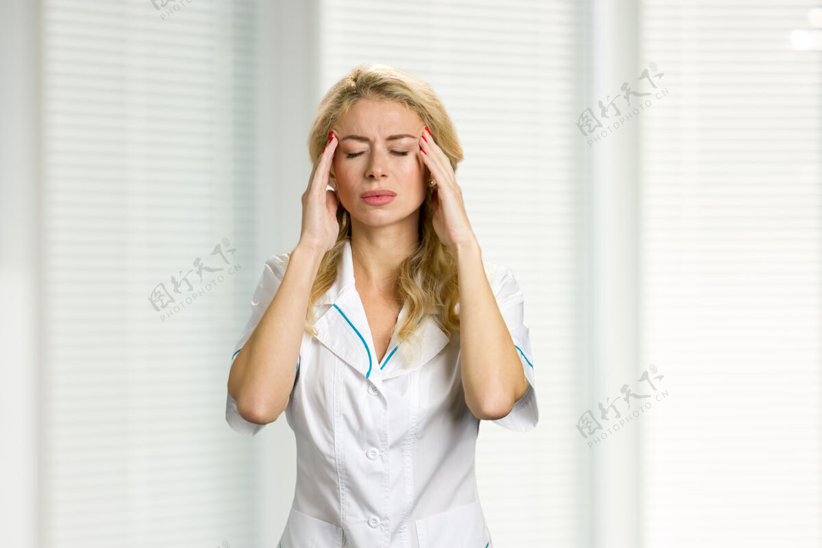 诊所头痛剧烈的年轻护士解开年轻护士或女医生的手 闭上眼睛放在颧骨上工作疼痛治疗