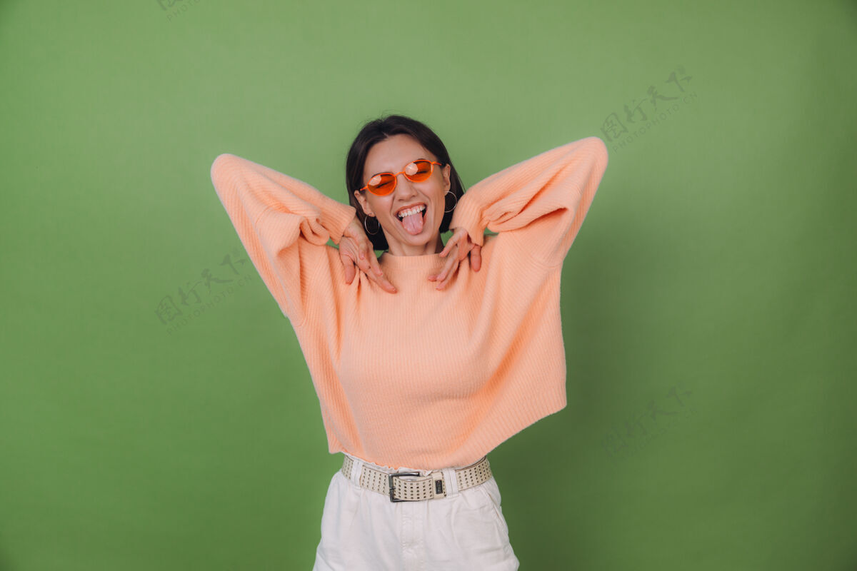 眼镜穿着休闲桃色毛衣和橘色眼镜的年轻时尚女性 隔离在绿橄榄色的墙上 快乐 积极 有趣地在复制空间里跳跃情感成人微笑