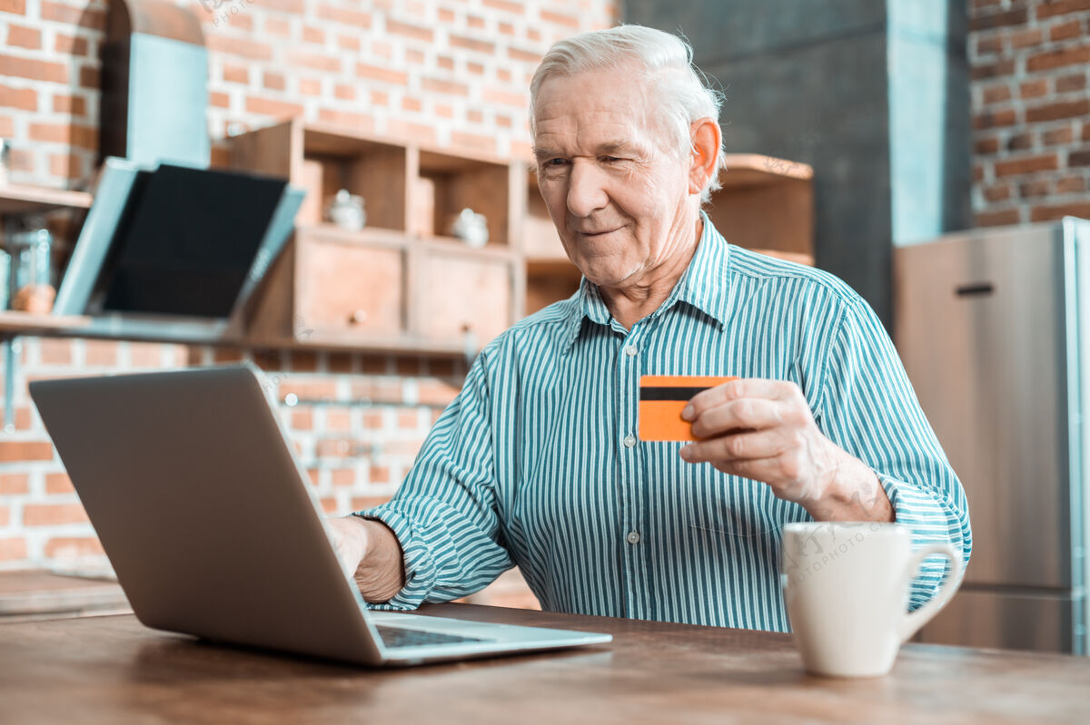 人快乐又好的老人微笑着看着笔记本电脑屏幕 同时使用他的信用卡保险休闲支付