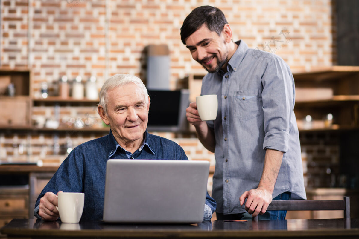 金融儿子站在附近时 一位积极的老人正在用他的笔记本电脑通信快乐成人