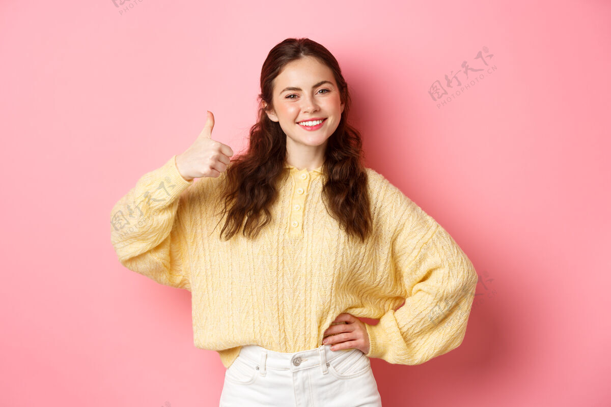 时尚自信微笑的女孩形象表示支持 竖起大拇指表示赞同 喜欢并同意你 称赞好的选择 站在粉红色的墙上赞成微笑喜欢