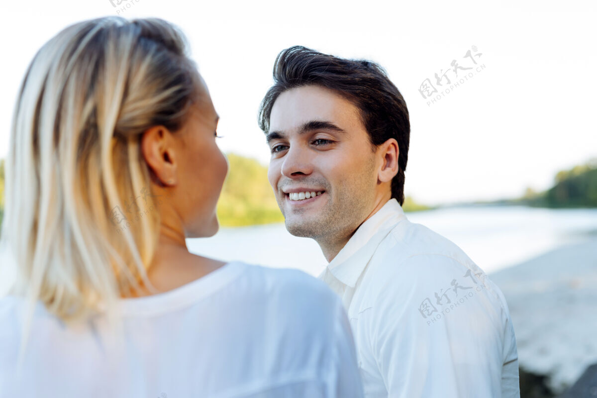 浪漫浪漫的时刻到了开朗的帅哥和妻子坐在河边 对她微笑着享受女性放松