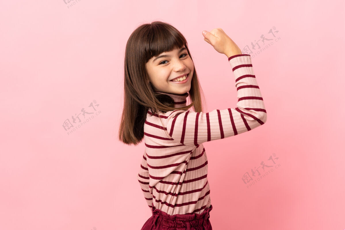 自信小女孩孤零零地站在粉红色的墙上做着坚强的手势墙乐趣人