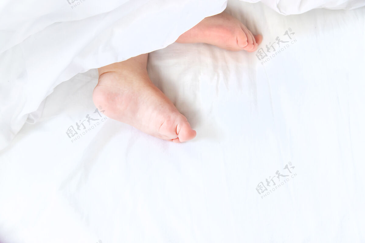 床宝宝用脚睡在白色的床上父母孩子可爱