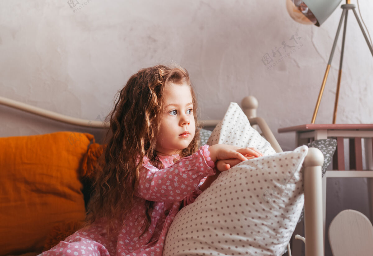 思考一个悲伤的小女孩坐在卧室的床上 看着窗外窗口.子对象的情绪忧郁心情童年室内肖像