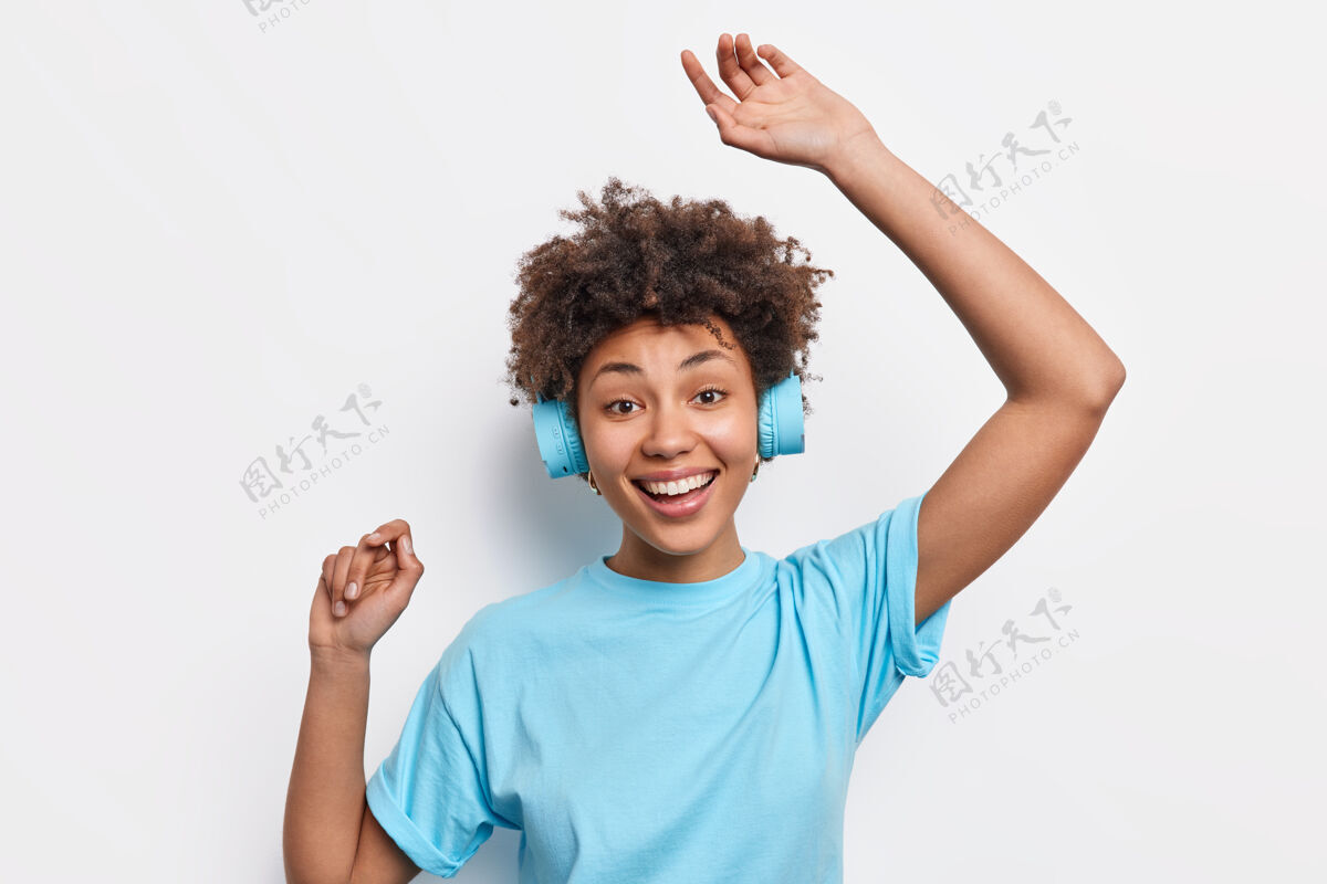 立体声有趣快乐的黑皮肤美国黑人年轻女子 穿着休闲的基本款t恤 随着音乐的节奏跳舞 戴着立体声耳机 隔着白墙人们喜欢生活方式 爱好概念积极民族乐观