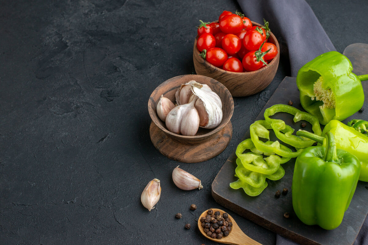 番茄正面近距离观看整个切好的切好的青椒 放在木制砧板上 番茄放在碗里 大蒜素放在黑色毛巾上 黑色表面蔬菜开心果食品