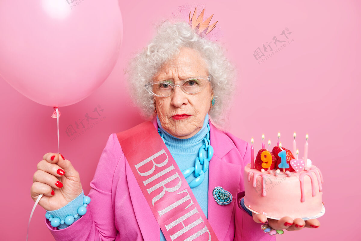 老年人严肃祖母的肖像庆祝91岁生日手持美味的蛋糕点燃蜡烛充气气球身着节日盛装看起来很悲伤 因为年龄大了蛋糕老年人老年人