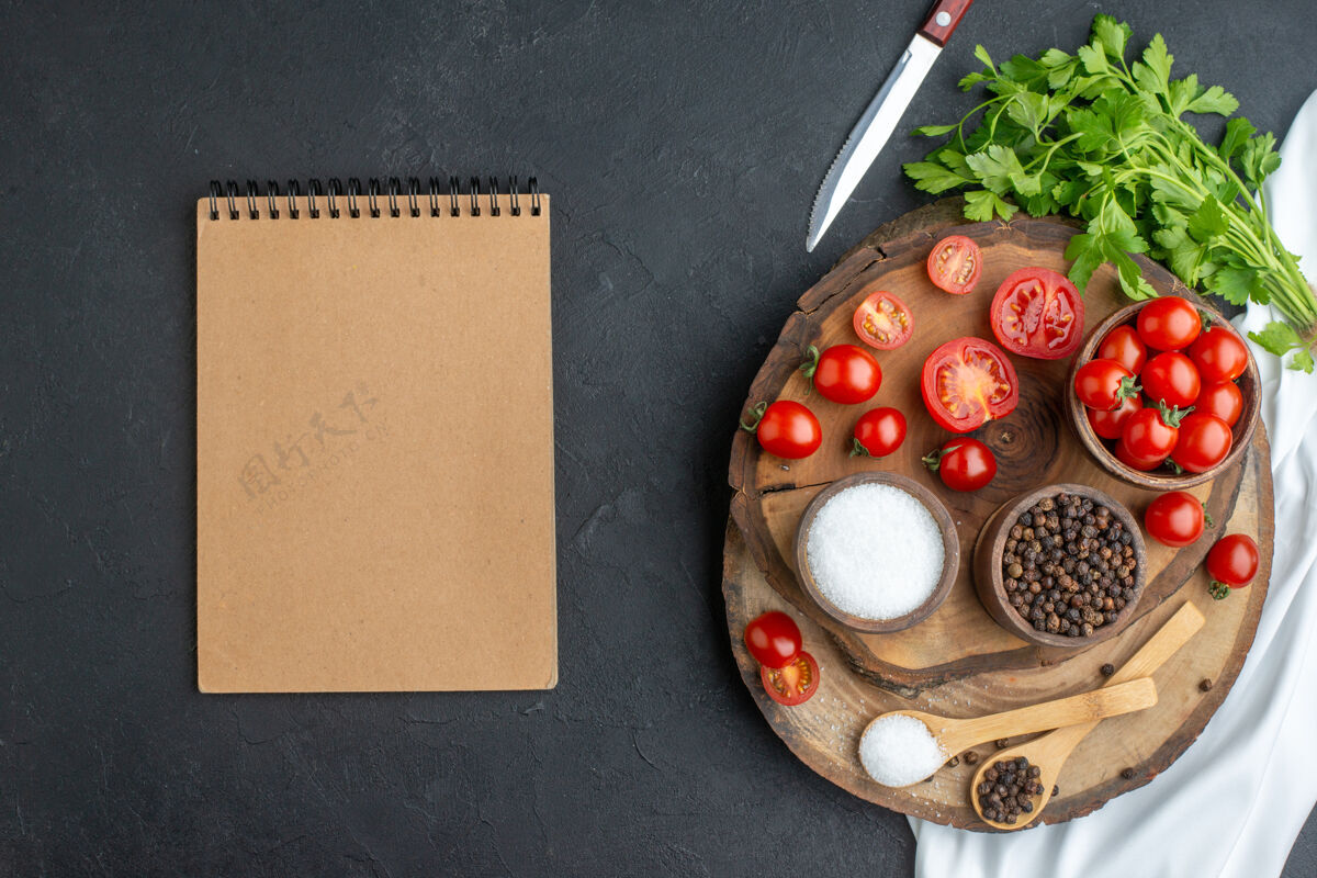 板上图：新鲜西红柿和香料放在碗里 勺子放在木板上 笔记本放在黑色的表面上笔记本马拉卡斯勺子