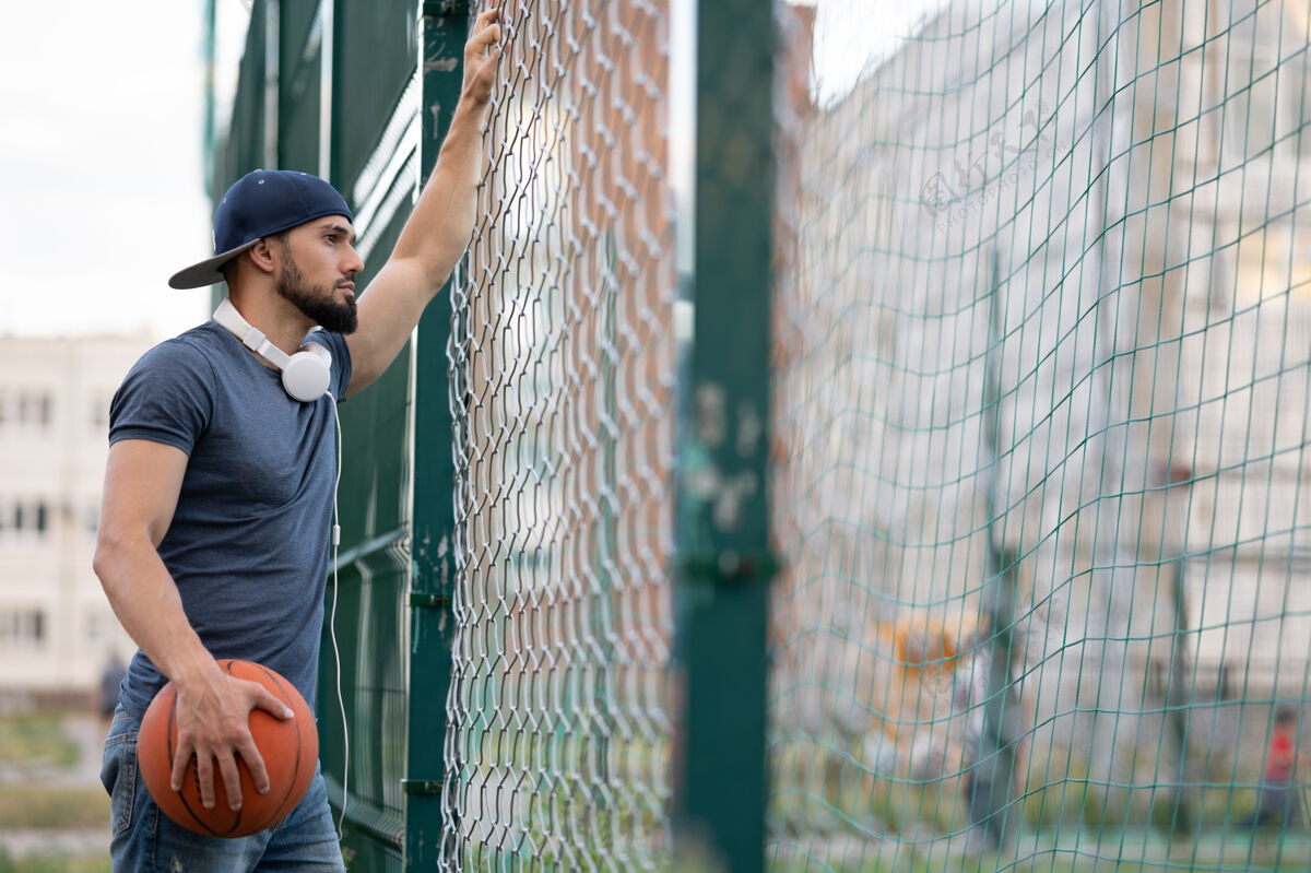 专业白天 一个拿着篮球的人从街上的篱笆后面往外看年轻户外能量