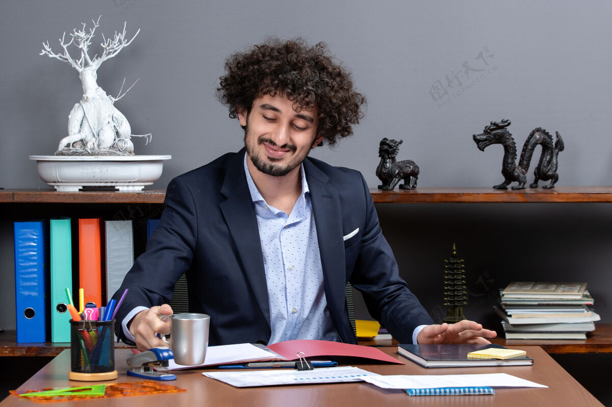 行政坐在办公室办公桌前微笑着喝茶的商人的正面视图主任办公室工作