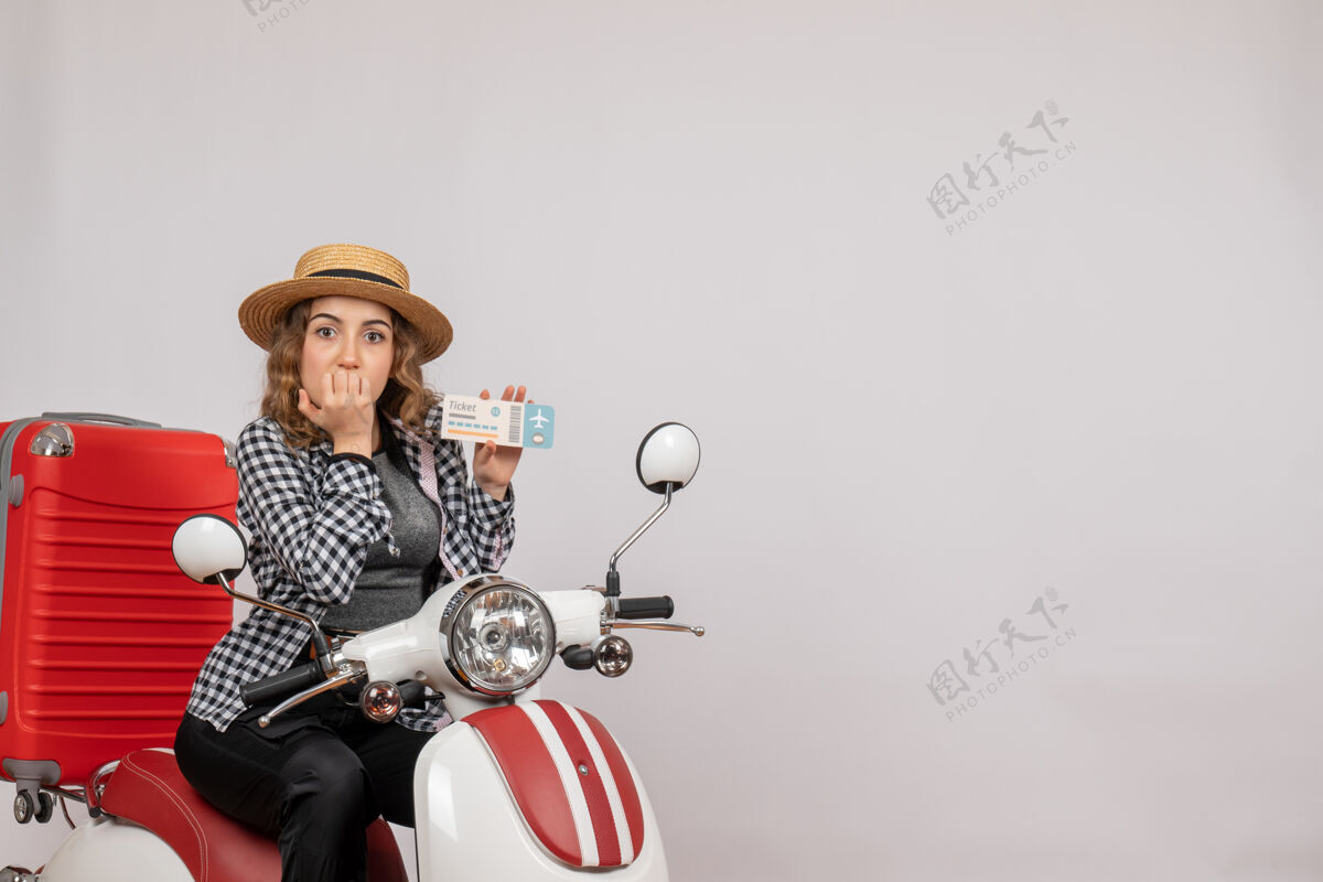 女人前视图骑着轻便摩托车的年轻女子举着旅行票旅游手提箱度假