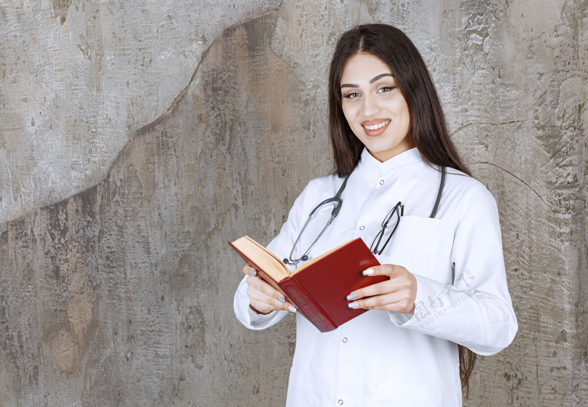 医院微笑的年轻女医生在灰墙上看书疾病听诊器治疗师