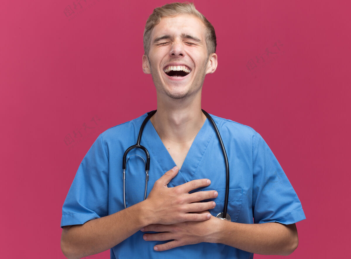 大笑闭着眼睛笑年轻男医生穿着医生制服听诊器隔离在粉红色的墙上姿势穿着公民