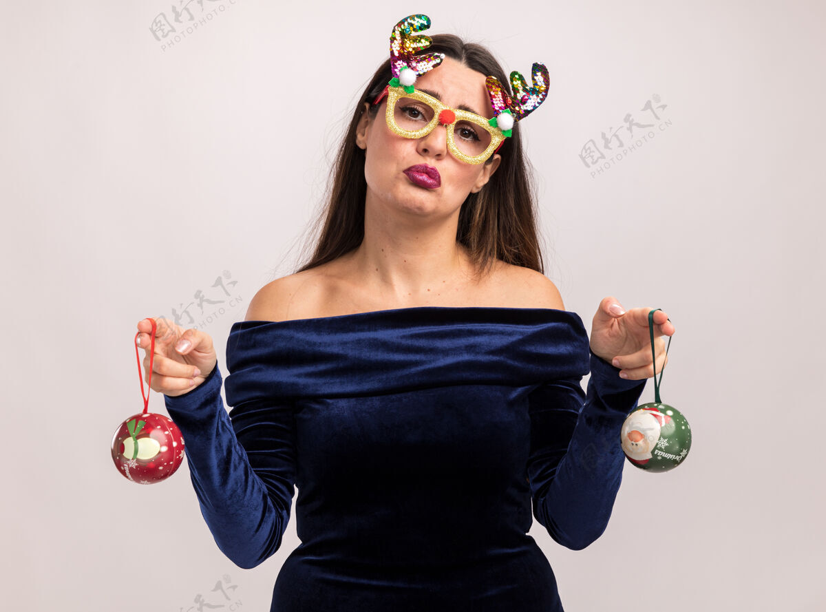 女孩悲伤的年轻漂亮的女孩穿着蓝色的裙子 戴着圣诞眼镜 手里拿着圣诞球孤立在白色的墙上舞会举行眼镜