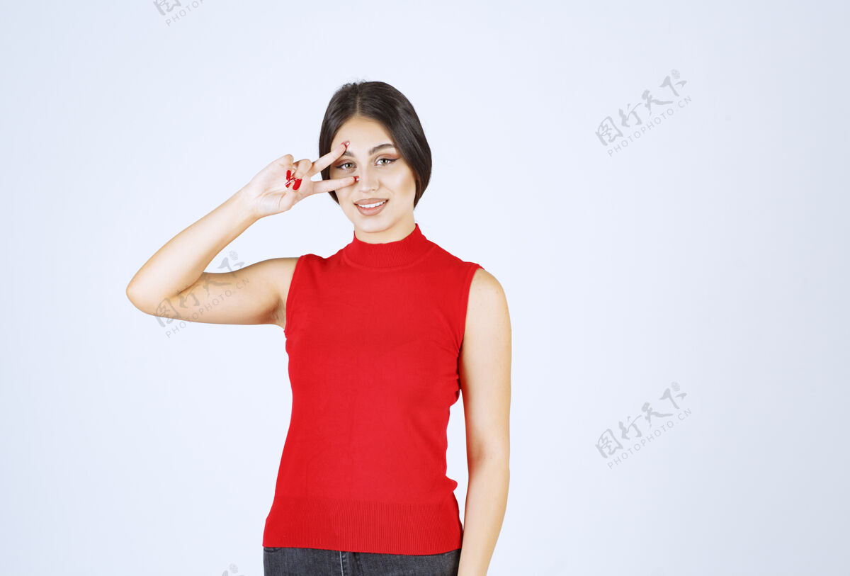 休闲穿红衬衫的女孩透过手指看隐私姿势女性