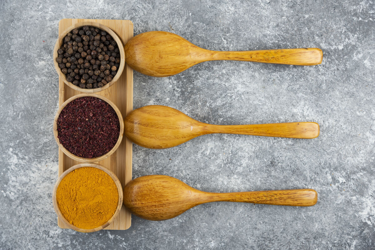 木板灰色桌子上放着不同的调味品和木勺切的胡椒粉红胡椒