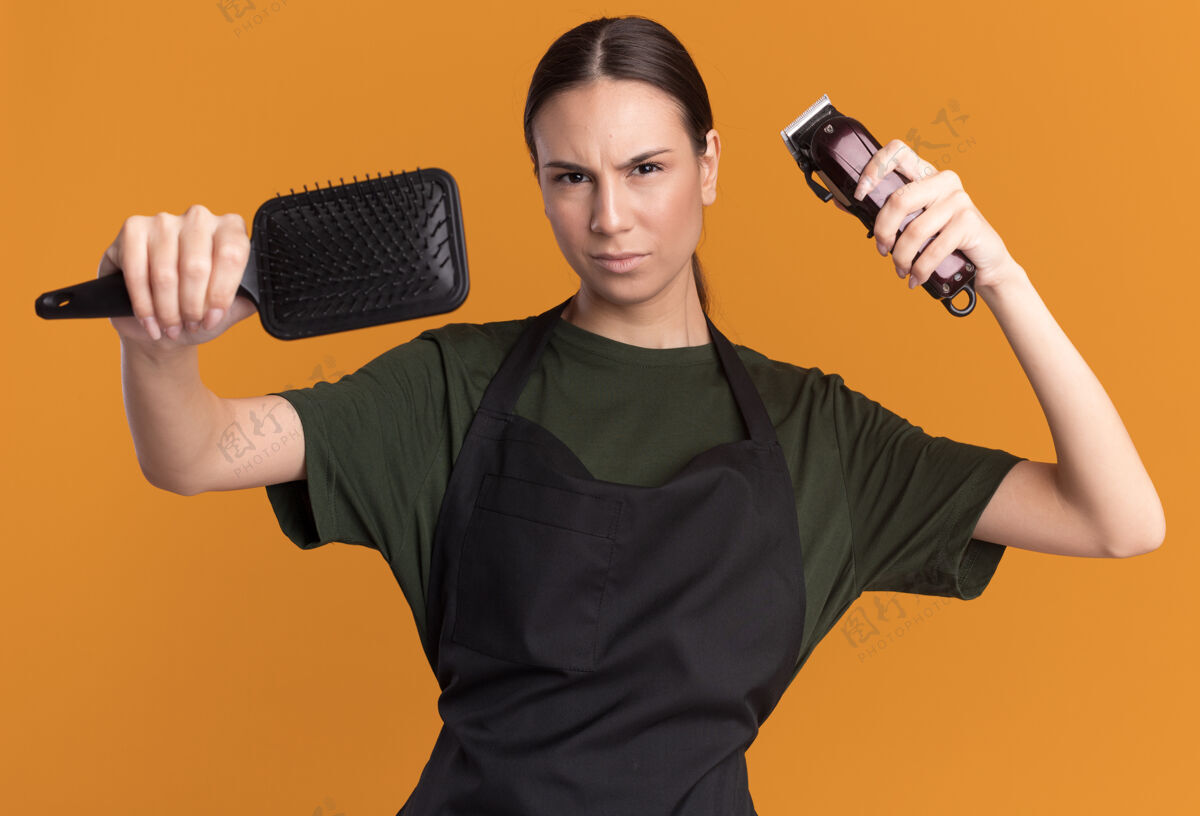 剪子严肃的年轻黑发女理发师穿着制服拿着理发器和梳子深褐色制服梳子