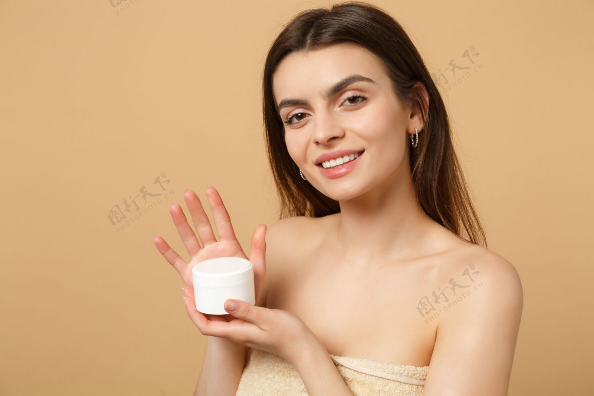 新鲜近景半裸体女人完美皮肤裸妆涂抹面霜隔离在米色粉彩墙上健康女人人