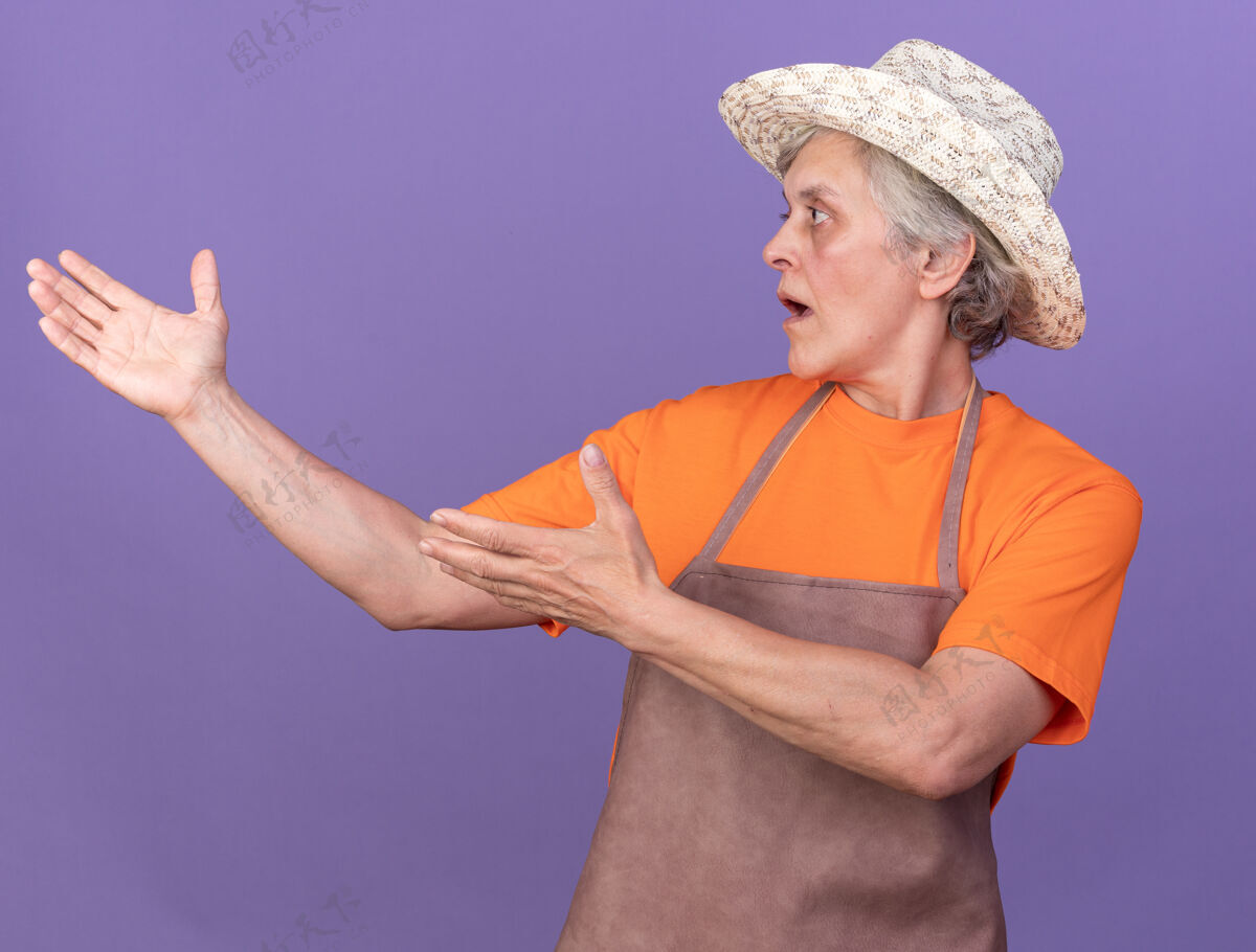 女震惊的上了年纪的女园丁戴着园艺帽看着并指着旁边园艺指紫色