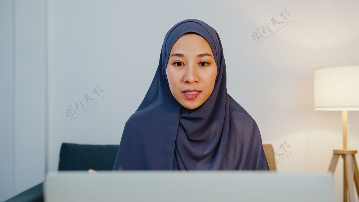 自由职业者穆斯林女士戴头巾用笔记本电脑和同事在视频电话会议上谈论计划 而远程工作在家里晚上在客厅女性围巾聊天