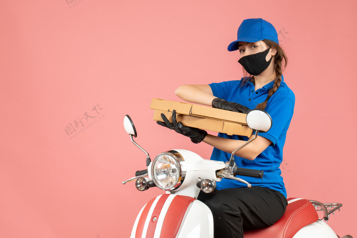 手套俯视图繁忙的女快递员戴着医用面罩和手套坐在滑板车上传递粉彩桃色背景下的订单头盔订单坐