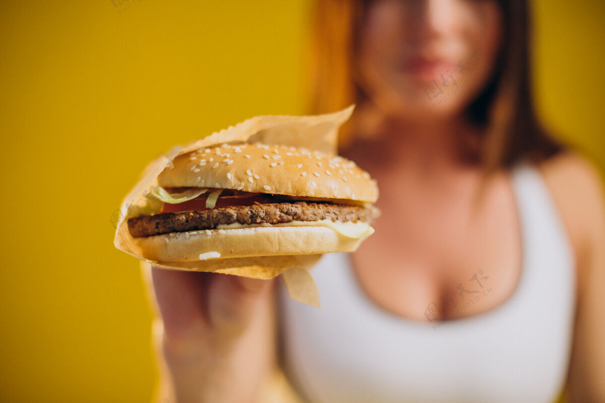 肉穿着运动服的女人吃着黄色背景的汉堡垃圾垃圾食品三明治