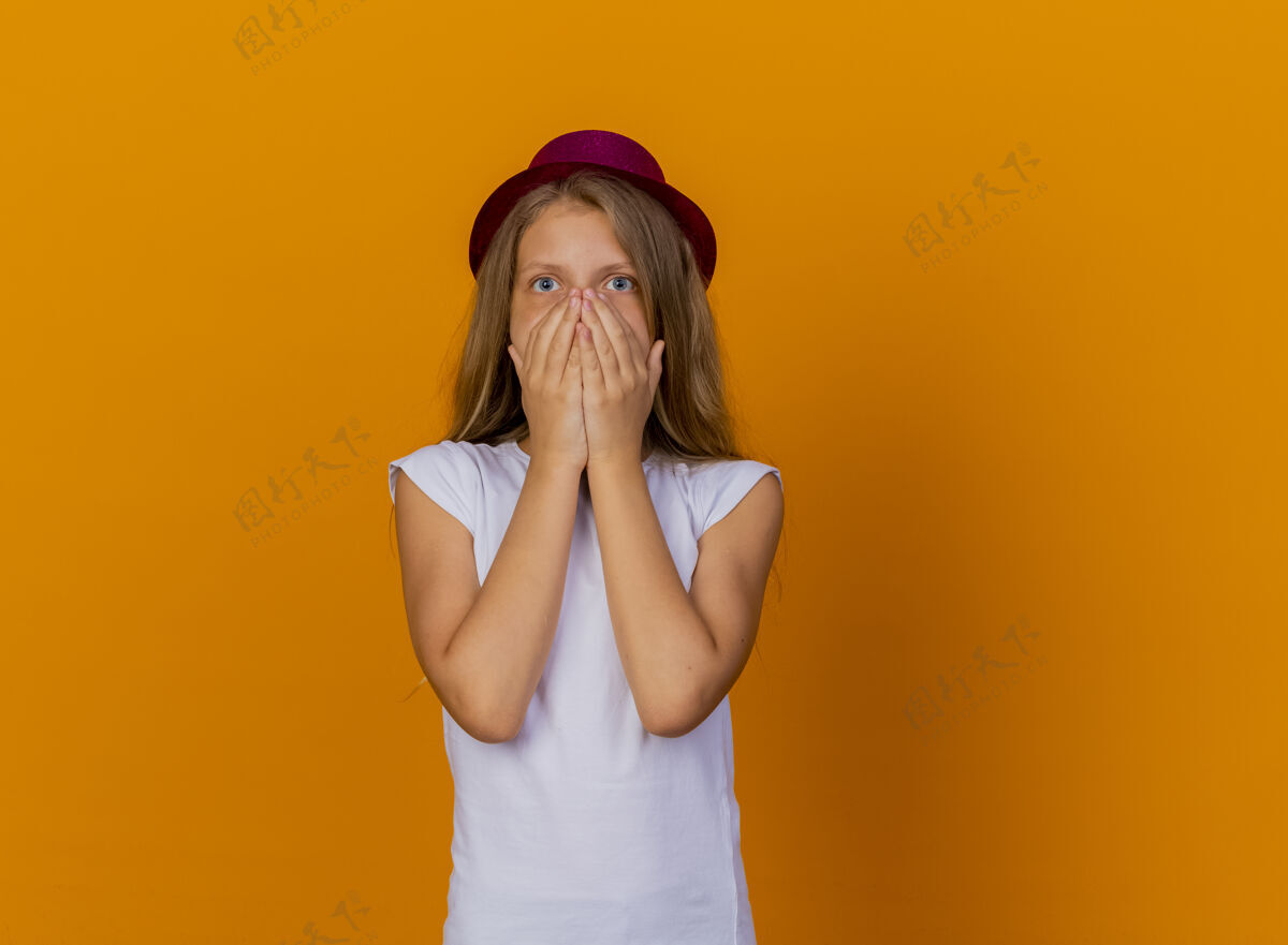 手戴着节日礼帽的漂亮小女孩被震惊了 双手捂着嘴 生日派对的概念嘴巴站封面