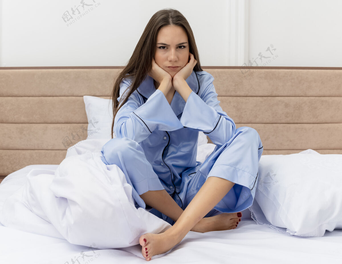 床穿着蓝色睡衣的年轻美女坐在床上 卧室里充满了悲伤的表情相机美丽灯光