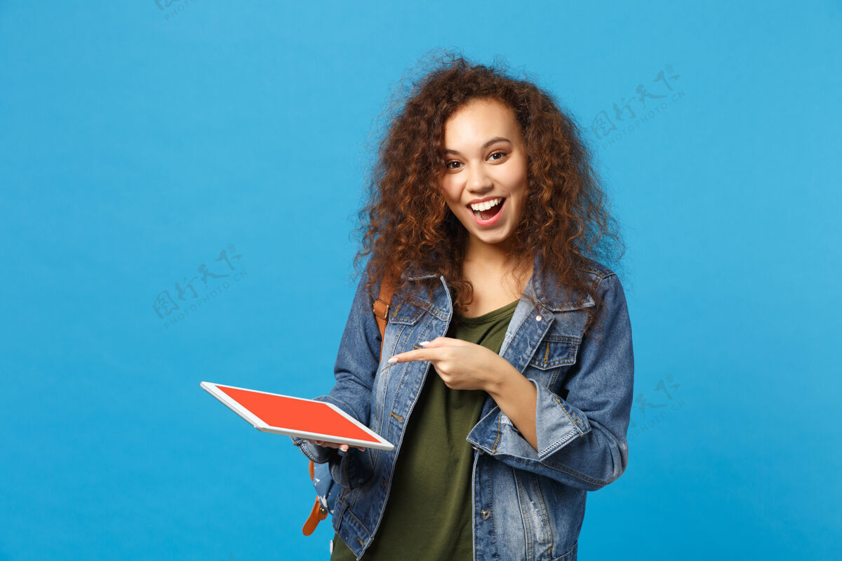 学生年轻的非洲裔美国女孩十几岁的学生在牛仔服装 背包举行垫电脑隔离在蓝色的墙壁上包显示器立场
