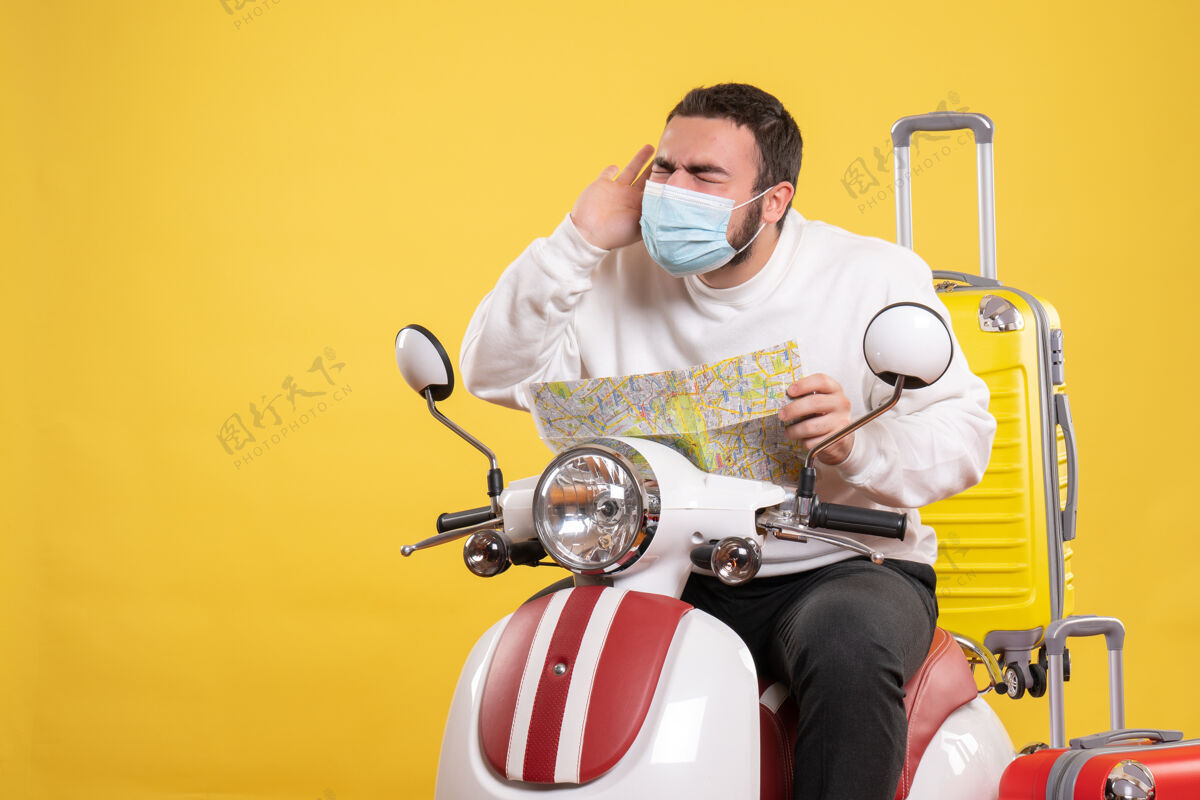 黄色一个戴着医用口罩的年轻人坐在摩托车上 背着黄色手提箱 手里拿着地图 头痛不已头痛面具地图