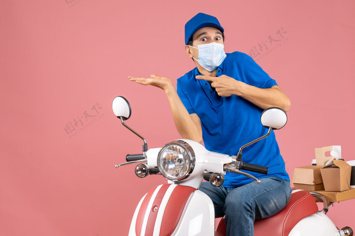 面具顶视图惊讶的送货员戴着医用面罩 戴着帽子坐在粉彩桃色的滑板车上男人惊喜